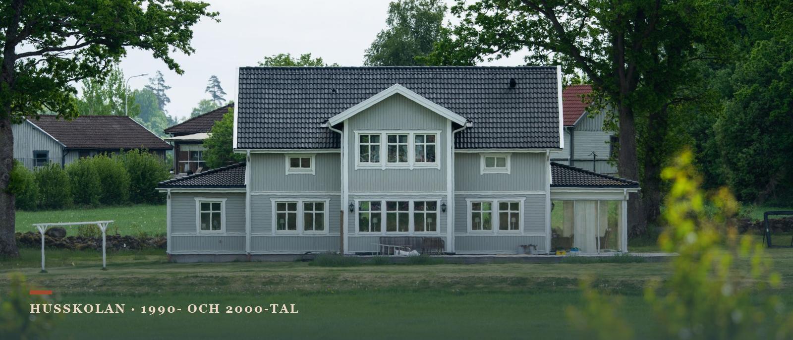 Grågrön villa i trä med vita foder, svarta betongpannor och inglasat uterum