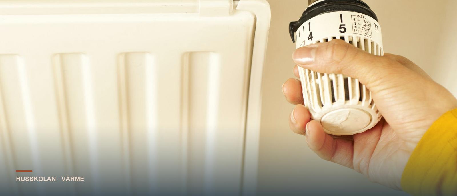 Hand justerar termostaten på en radiator för vattenburen värme